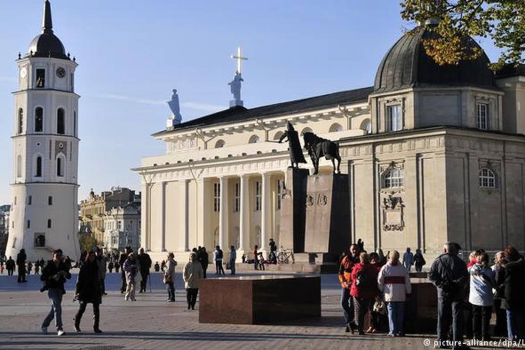 A foto mostra a praça em frente à catedral de Vilnius bastante movimentada durante uma tarde.