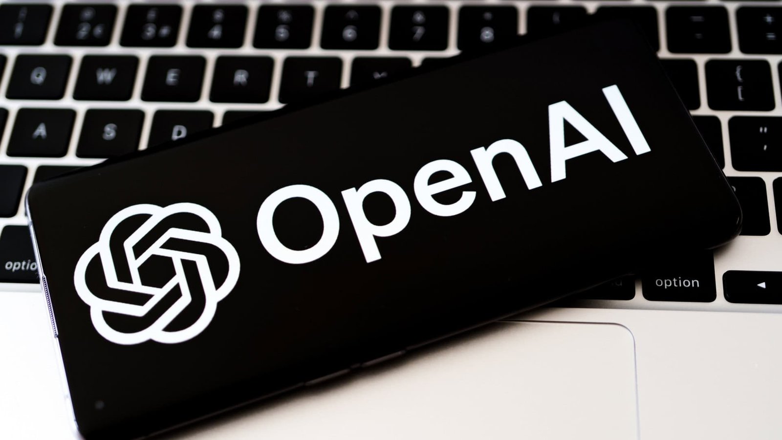 Logo da OpenAI em um smartphone que está em cima do teclado de um notebook