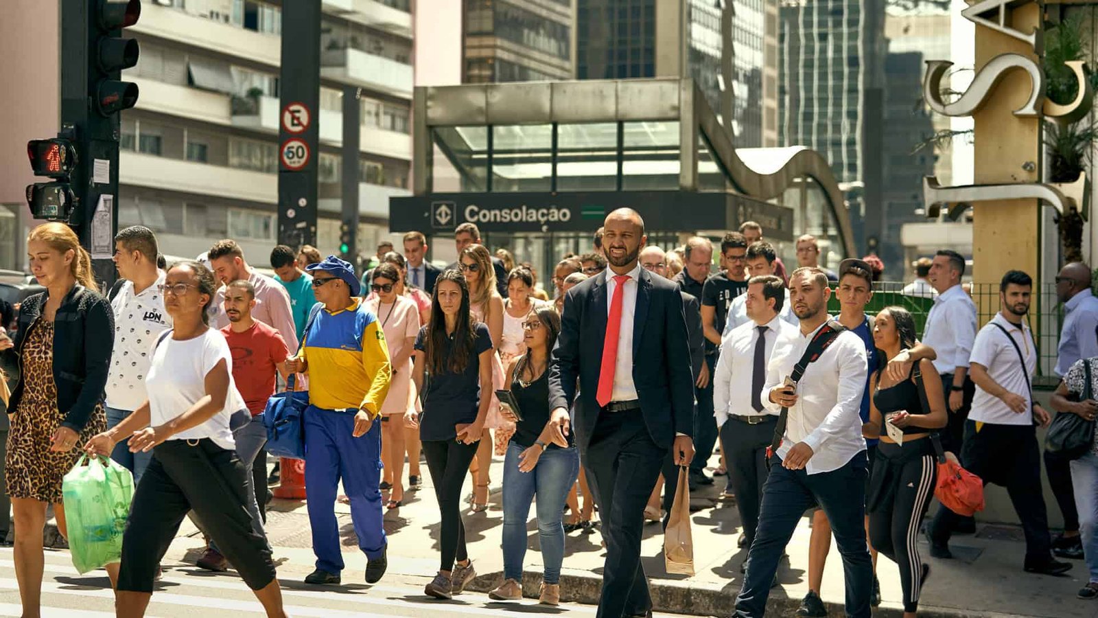 Várias pessoas atravessando a rua em frente a uma estação de metrô