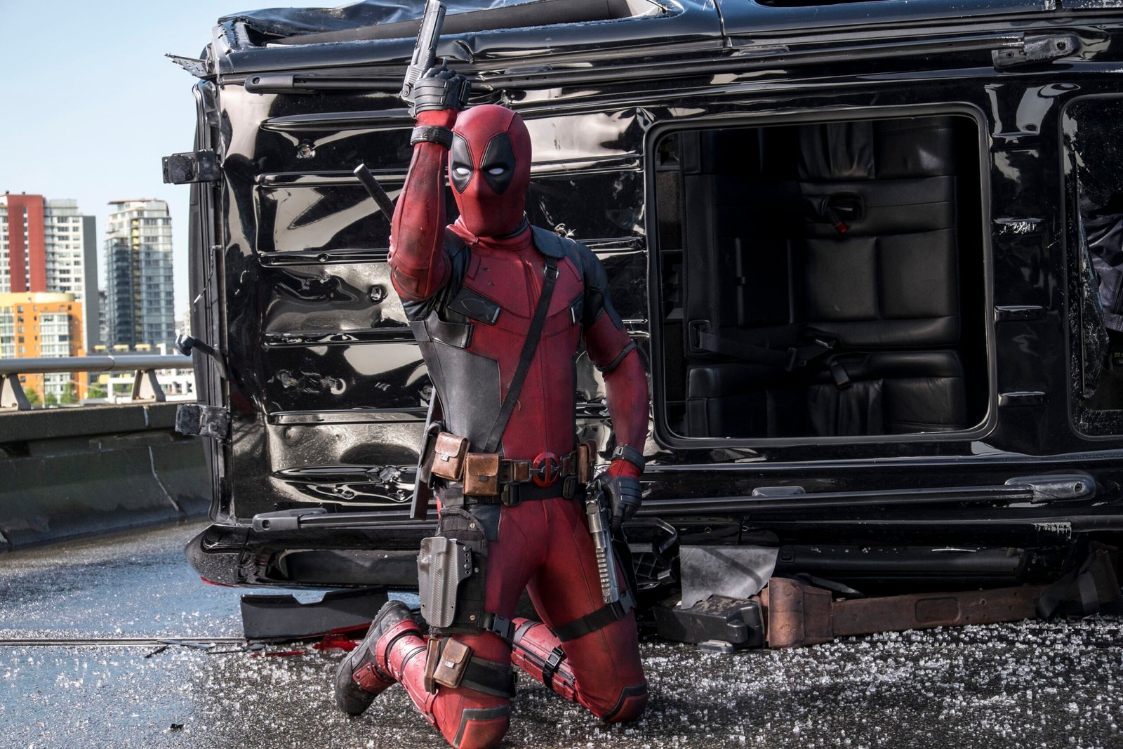 deadpool-filme-heroi-ajoelhado-em-cena-de-acao-com-veiculo-destruido-ao-fundo