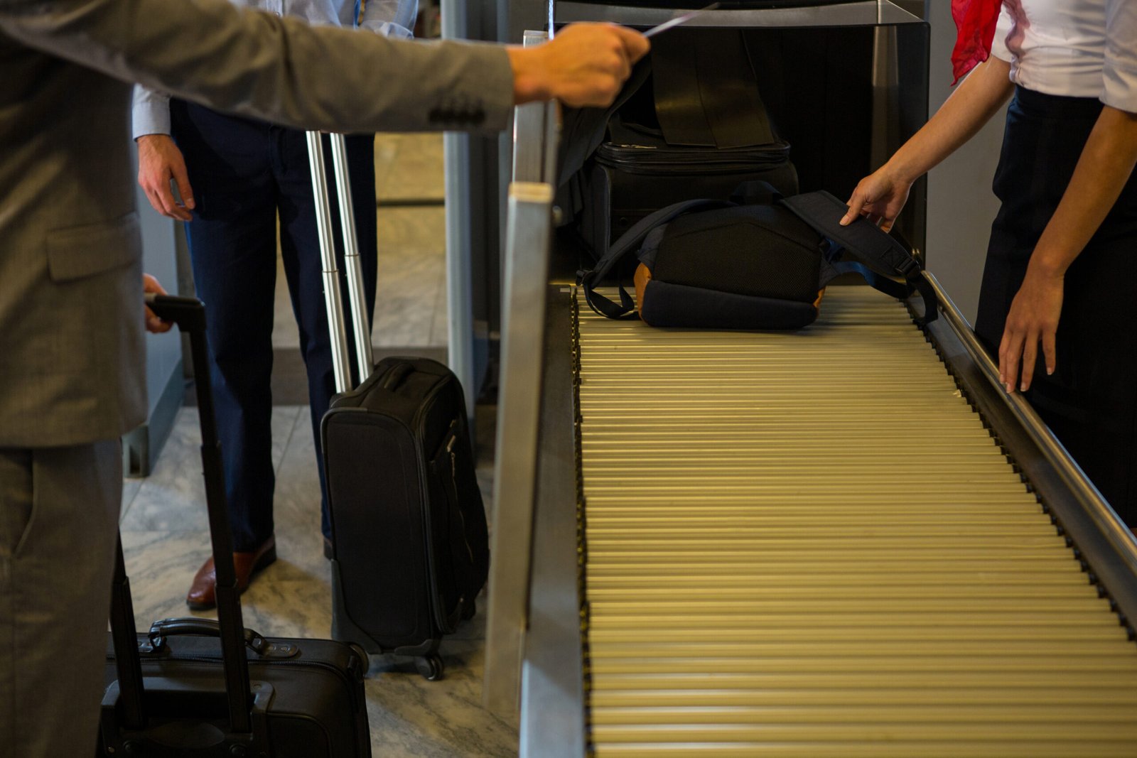 Female staff checking passengers luggage on conveyor belt in airport