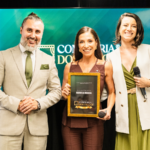Marcela Brasca recebe reconhecimento no palco da Confraria dos Palcos ao lado dos organizadores durante evento de formação de palestrantes