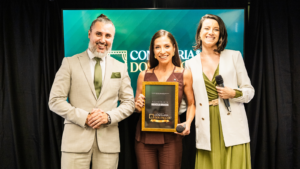 Marcela Brasca recebe reconhecimento no palco da Confraria dos Palcos ao lado dos organizadores durante evento de formação de palestrantes